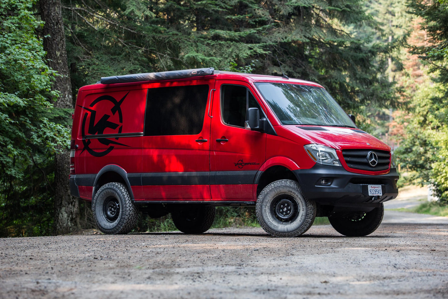 Red van equipped with Stage 5 System, 2 lift from Van Compass, parked on gravel road, showcasing improved ground clearance for Sprinter 4x4 (2015-2018 2500).