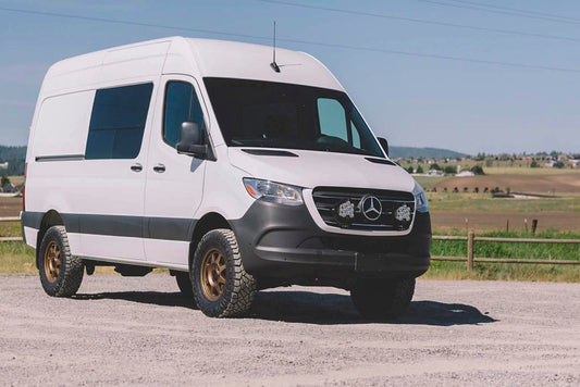 White van featuring the STAGE 5 SYSTEM, 2 LIFT - SPRINTER 2WD (2019+ 2500 ONLY) by VAN COMPASS, parked on a gravel road.
