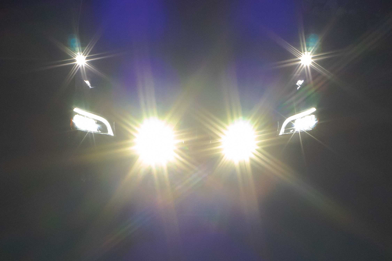 Close-up of a Sprinter van headlight with bright light lens flare on a dark background.