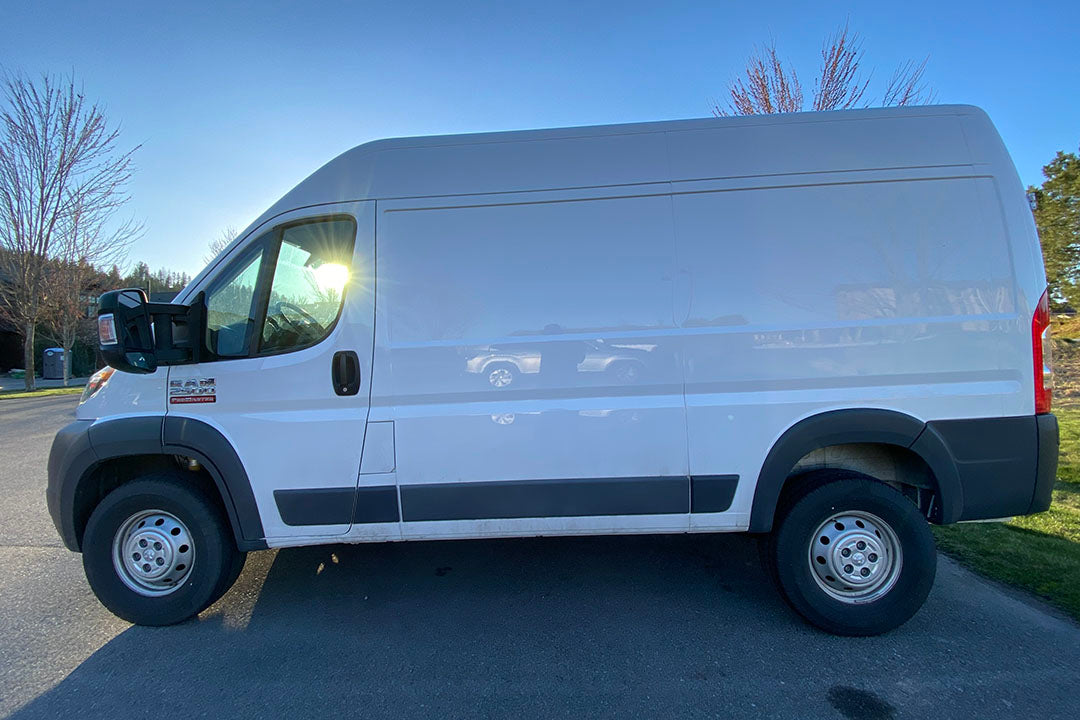 A white van is parked in a lot, with close-ups of its tires and side view mirror visible.