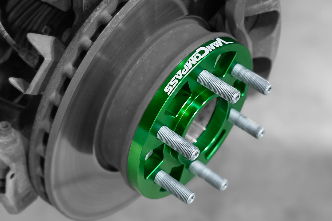 A detailed image of a 14mm wheel spacer, showcasing a green anodized aluminum spacer attached to a vehicle hub, with adjacent parts in grayscale for a striking contrast.