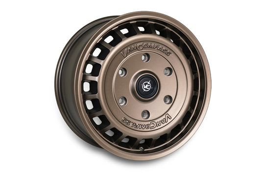 A single metallic bronze-colored van wheel rim with a multi-spoke design and cutouts, featuring the 'Van Compass' brand name and logo embossed on the center cap, set against a plain white background.