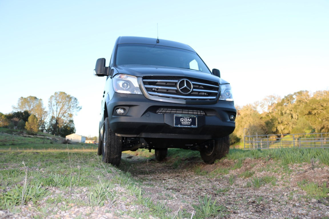 Sprinter 4x4 van featuring the Van Compass Engine Skid Plate, designed for off-road protection with durable aluminum and steel construction, parked on a grassy field.