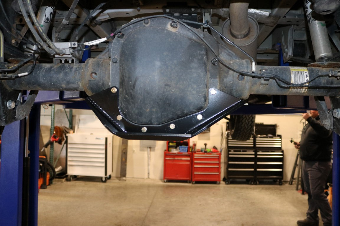 Differential skid plate by Van Compass under a vehicle in a garage, showing its robust 1/4 steel construction designed to protect the rear differential.