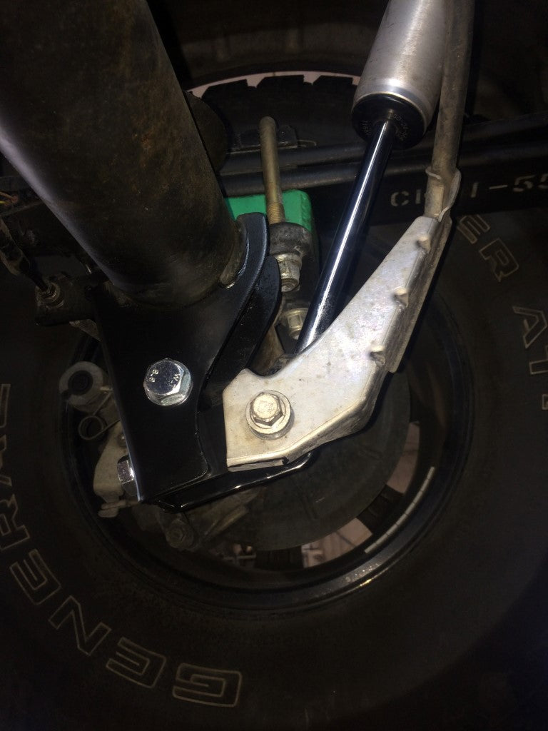 Close-up of REAR HIGH CLEARANCE SHOCK EXTENSION BRACKETS - TRANSIT (2013+) by VAN COMPASS, showing the detailed bolt-on mount and screw for improved ground clearance.
